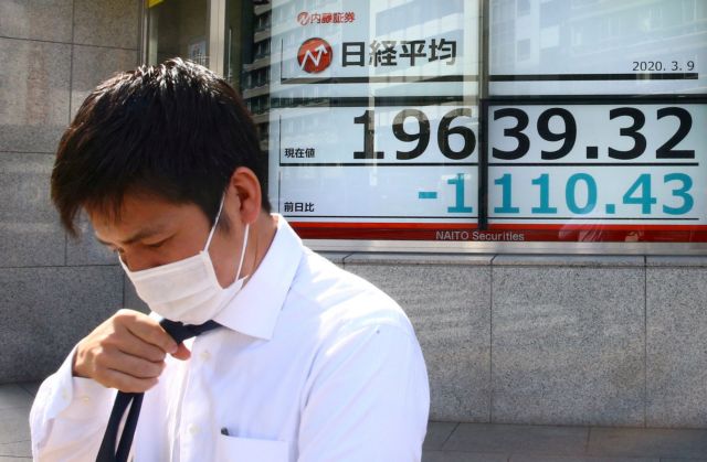 FILE PHOTO: A man wearing a protective face mask stands near an electronic display showing the Nikkei index following an outbreak of the coronavirus disease in Tokyo
